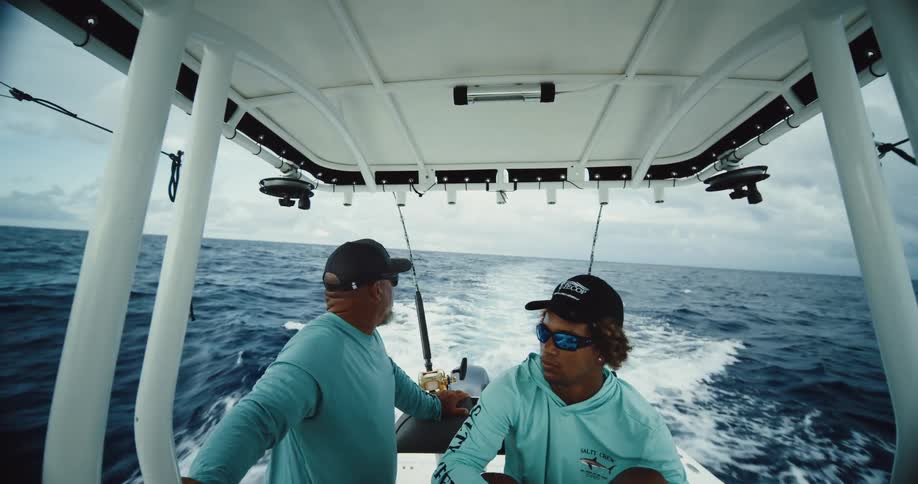 Two fishermen in a boat moving through the sea talk to each other