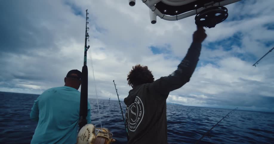Two men are working different fishing poles on the boat