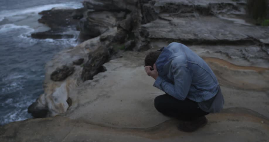 Man crouching down covering his face by the water