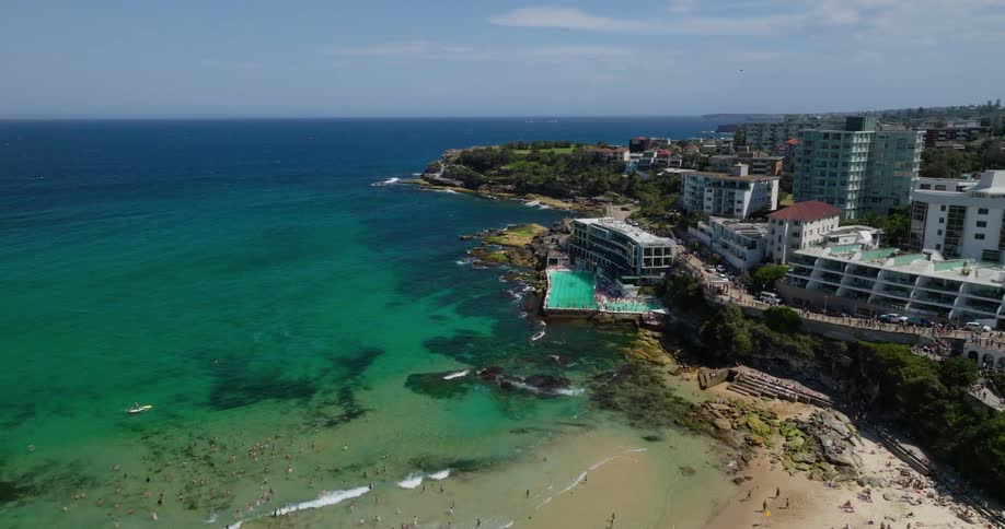 A coastal scene with turquoise waters rocky shores a large ocean pool and a residential area extending along the coastline