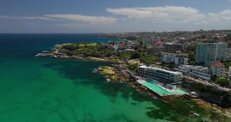 A coastal scene with turquoise waters rocky shores a large ocean pool and a residential area extending along the coastline