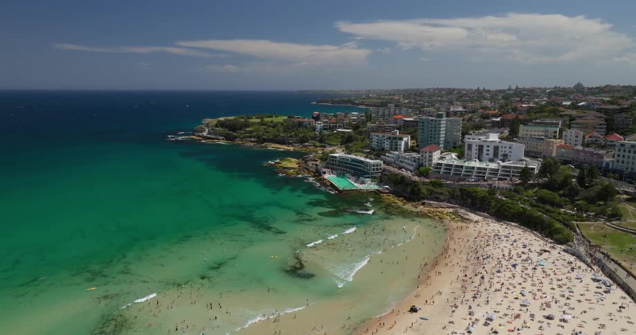 A coastal scene with turquoise waters rocky shores a large ocean pool and a residential area extending along the coastline