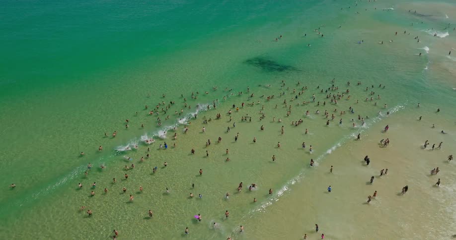 A crowded beach with people swimming and sunbathing in the shallow water