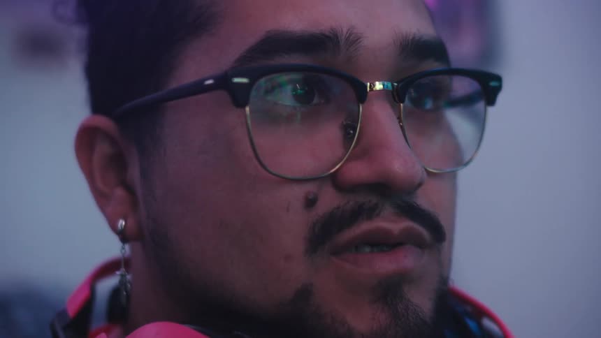 A person with short curly hair is wearing pink headphones around their neck and is focused on a video game