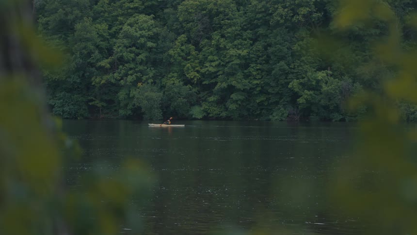 Person paddling a canoe on a river surrounded by forest