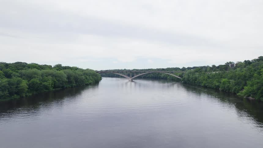Aerial view of a river surrounded by a forest and a bridge in the background