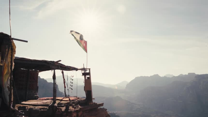 Flag flaps in the wind near a corner of a home at the edge of a cliff over a foggy valley