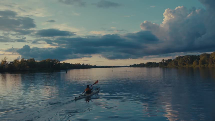 An adult kayaks on a river on a cloudy autumn morning