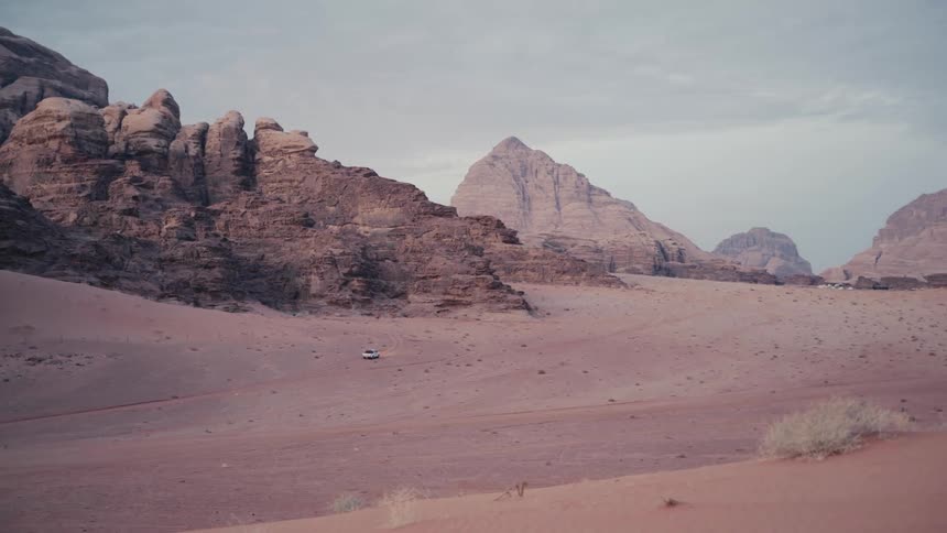 A car looks very tiny compared to the empty desert it is driving in