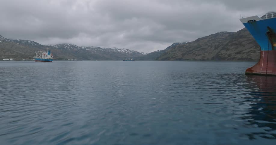 Three cargo ships on a body of water with a backdrop of gray mountainous terrain under a cloudy sky