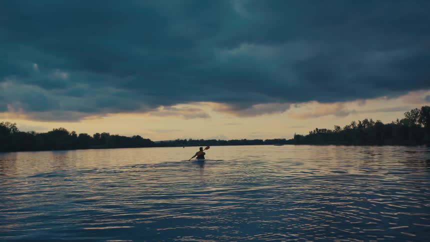 Silhouette of a person canoeing on a river at a cloudy dawn