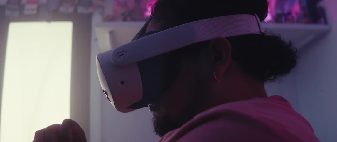 Man wearing a virtual reality headset puts on a controller while sitting on his bed