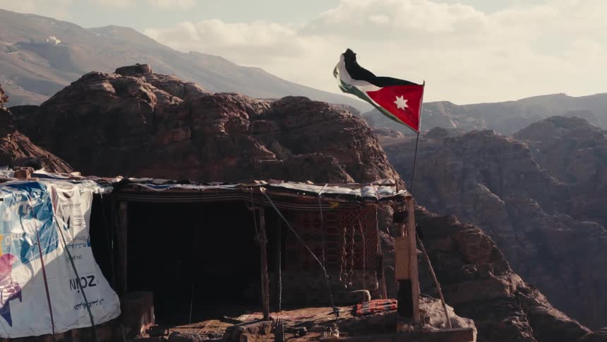 Jordanian flag framed by a majestic backdrop of rocky mountains and a humble shelter made of rustic materials