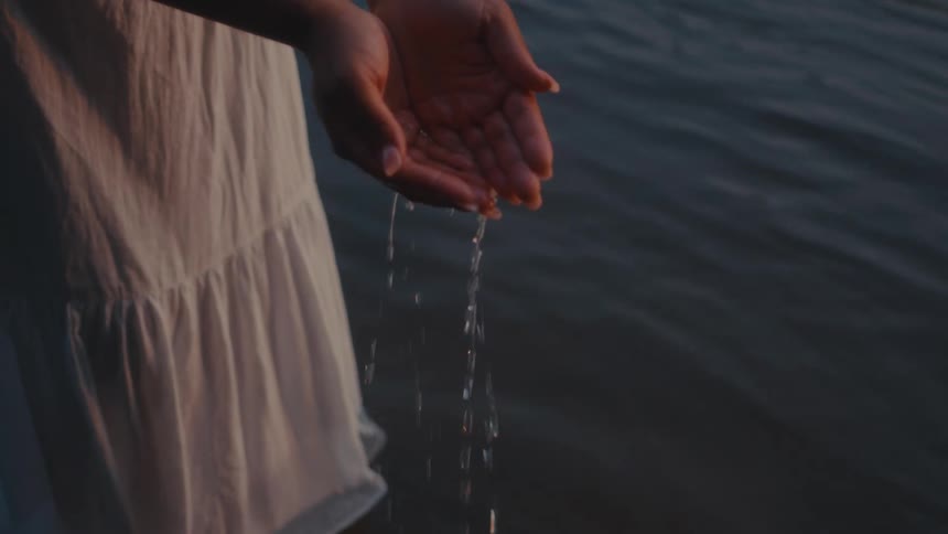 Close up of pair of hands of a woman in a wet white dress holding water