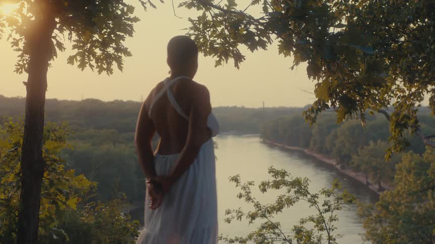 Woman stands at a high point and looks over a river and forest on a slightly foggy day