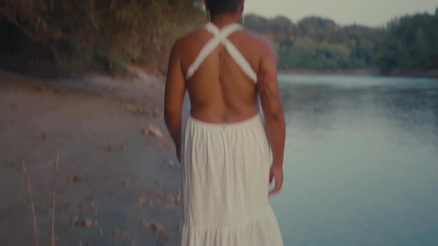 Person from behind walking in a white dress on the bank of a river