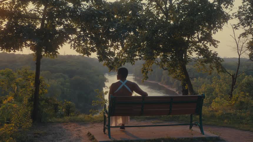 A woman sits on a bench that is overlooking a vast forest