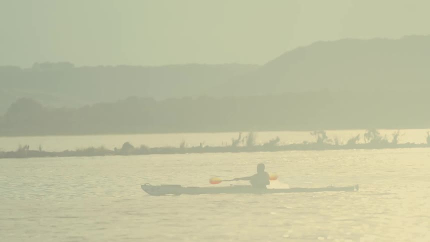 A person is kayaking on a calm body of water using a doublebladed paddle to propel a kayak forward