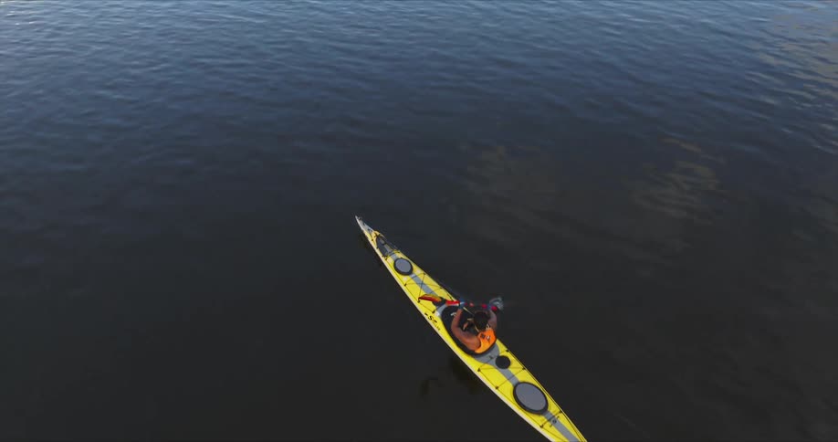 A person is kayaking on a calm body of water using a doublebladed paddle to propel a yellow kayak forward