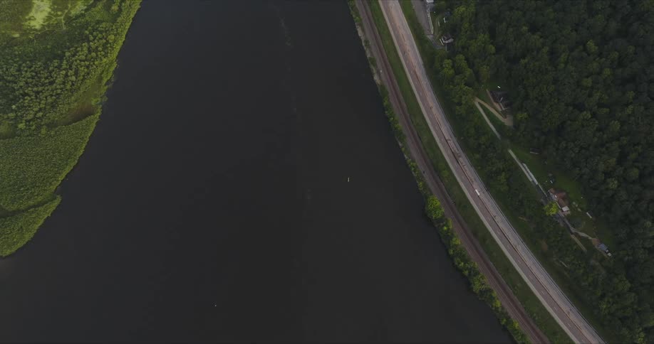 An aerial view shows a winding road running parallel to a river surrounded by lush vegetation