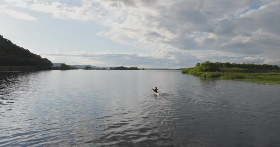 A person is kayaking on a calm body of water using a doublebladed paddle to propel a yellow kayak forward