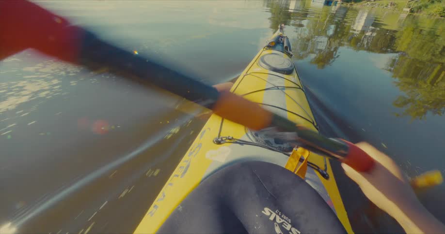 Someone paddling a yellow kayak through calm water using an orange tipped paddle
