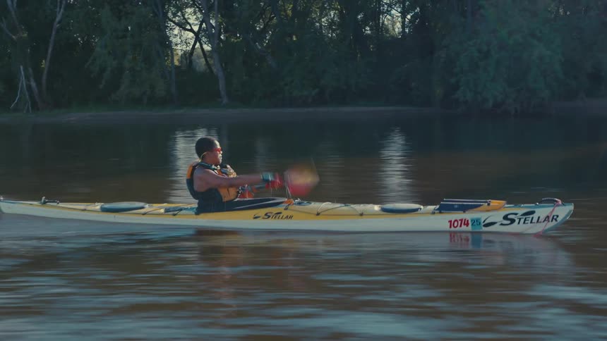 A person is kayaking on a calm body of water using a doublebladed paddle to propel a yellow kayak forward