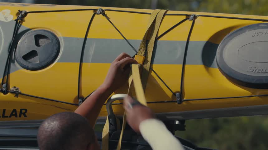 A person straps a kayak on the vehicle