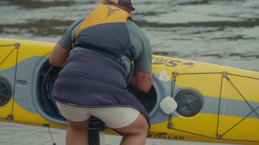 Person prepares to enter a vibrant yellow kayak on the edge of a river