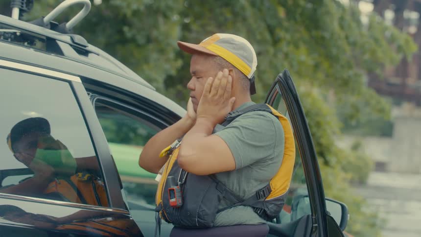 Woman in a vest rubbing her face while standing next to a car