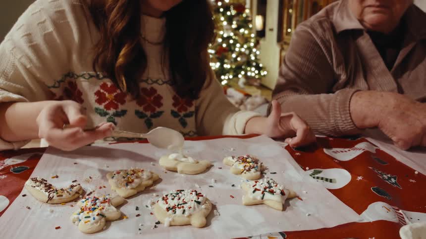 A persons hand using a spoon to spread white sauce over biscuits that are placed on a piece of paper on a table
