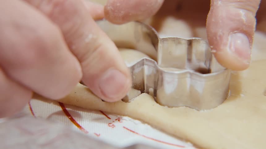 An adult cuts out homemade sugar cookies with a snowman cookie cutter