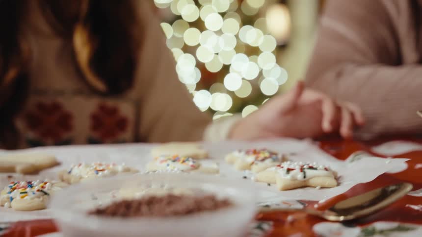 A family looking at a plate of decorated christmas cookies with colorful sprinkles on a table
