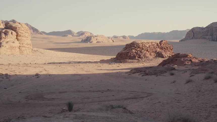 Car traveling in a desert environment with sparse vegetation and canyons