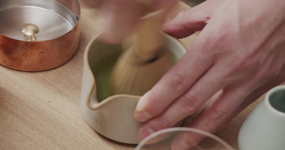 Hand with a bristle tool swirling a green liquid inside a mug