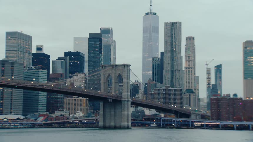 The brooklyn bridge stretches across the east river with the manhattan skyline towering in the background