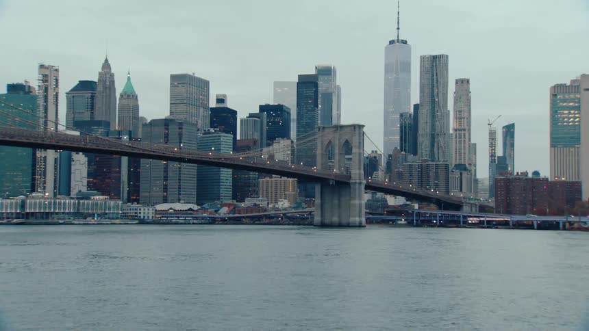 The iconic brooklyn bridge spanning a body of water with the new york city skyline in the background under an overcast sky