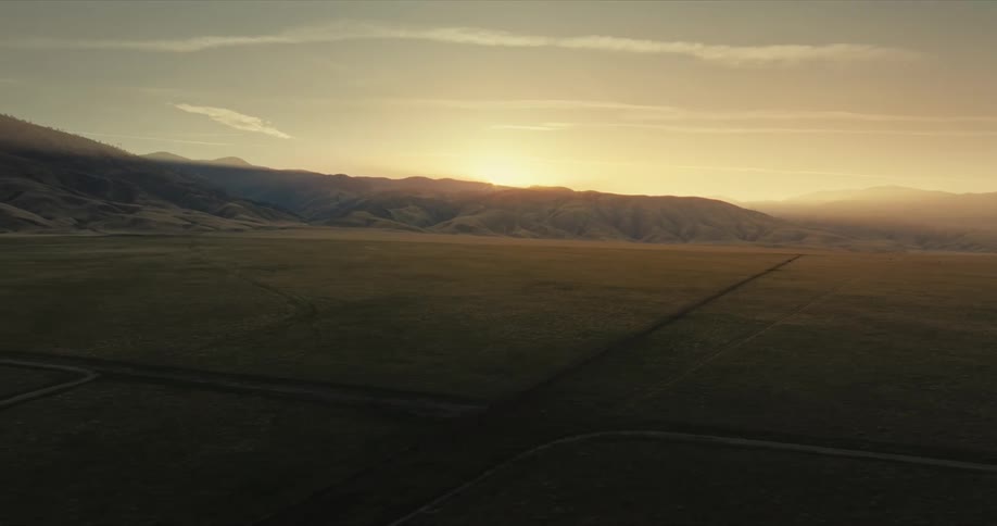Aerial view of a green field with mountains and the sun rising on the horizon