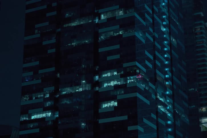 Lights turn off a modern glass skyscraper at night