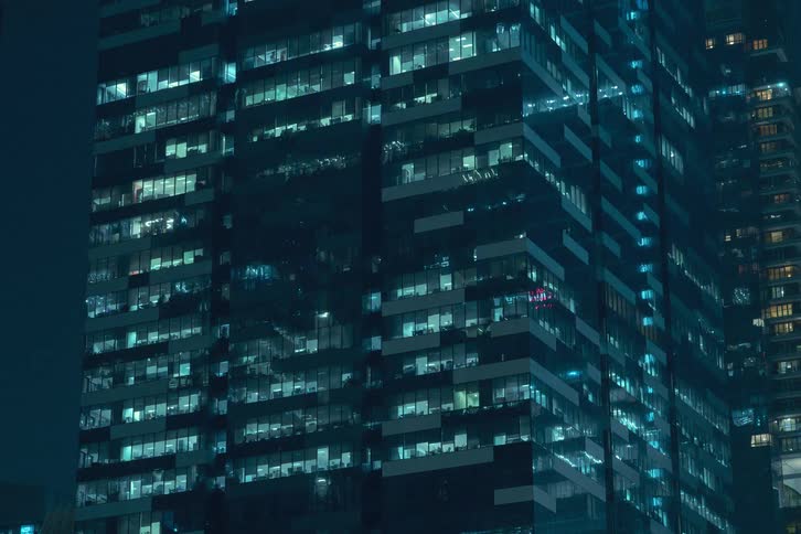 A skyscraper at night with countless illuminated windows creating a grid like pattern and flickering lights adding a sense of movement