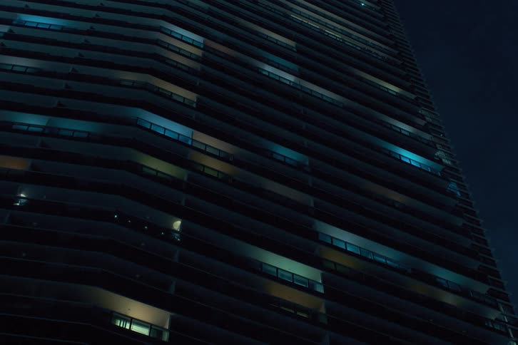 The facade of a modern highrise building at night with the windows turning off in a flickering pattern creating a dynamic grid like effect on the facade