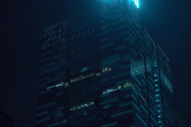 A towering skyscraper at night illuminated by a spotlight casting a dramatic glow against the dark sky before the lights turn off