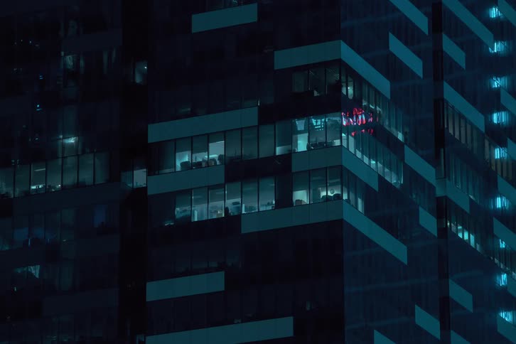 A skyscraper at night with countless illuminated windows creating a grid like pattern and flickering lights adding a sense of movement