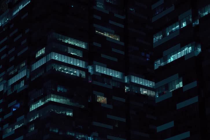 Lights turning off on tall skyscraper dominates the night sky its windows illuminated in a pattern that flickers and pulses casting an eerie glow on the surrounding area