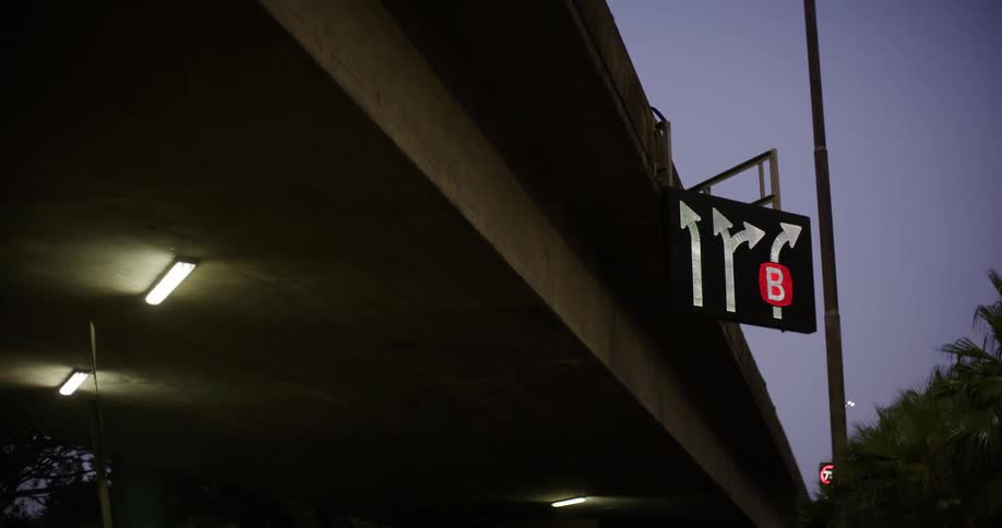 A road sign with arrows pointing in different directions under a bridge at night