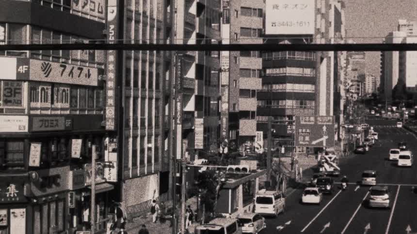 A busy urban street scene with multiple vehicles surrounded by tall buildings with signs and advertisements in japanese