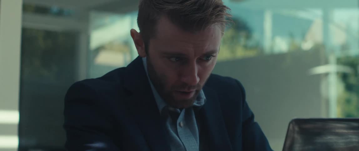 A man in a dark suit jacket and lightcolored shirt sits outdoors having a meeting on a laptop