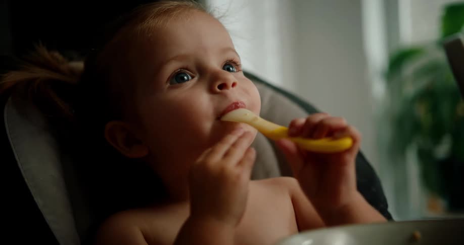 A baby girl eating oatmeal with a spoon