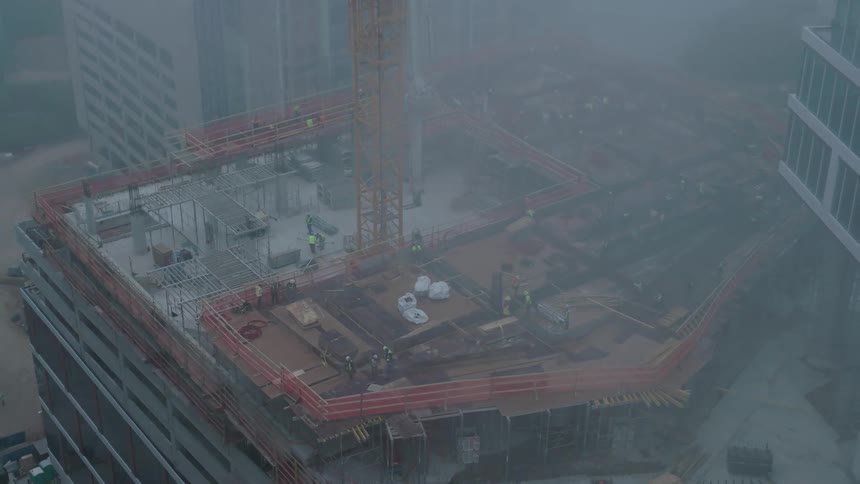 Construction workers work on a skyscraper being built downtown on a foggy day