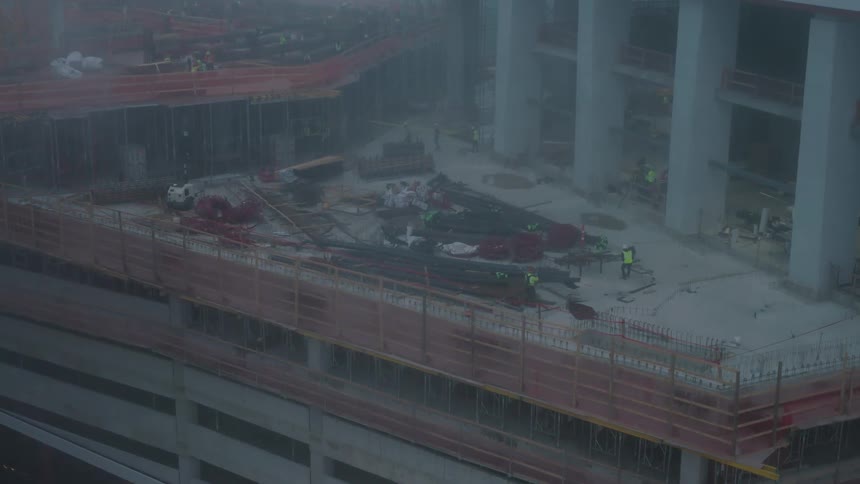 Group of builders in high visibility vest working on construction of skyscraper on a foggy day